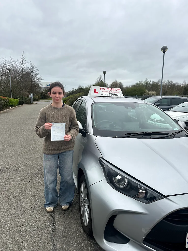 Successful driving pupil holding a pass certificate beside the Pass with Ash learner car.