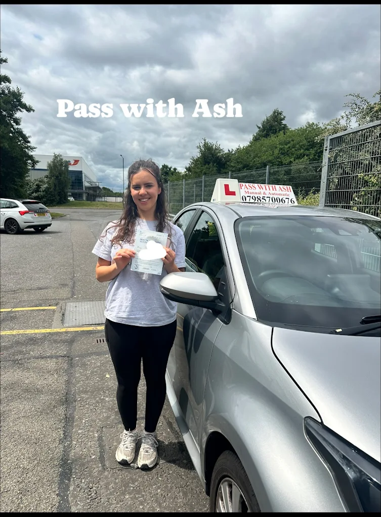 Learner driver smiling with pass certificate beside the Pass with Ash car.