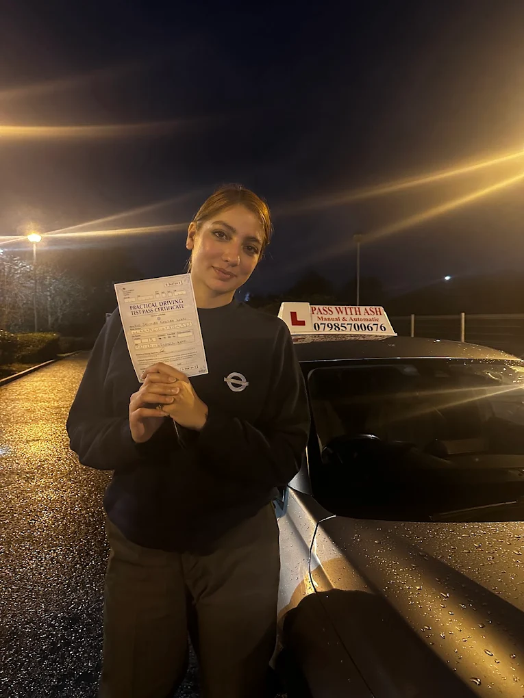 Pupil holding driving test pass certificate at night beside the Pass with Ash car.